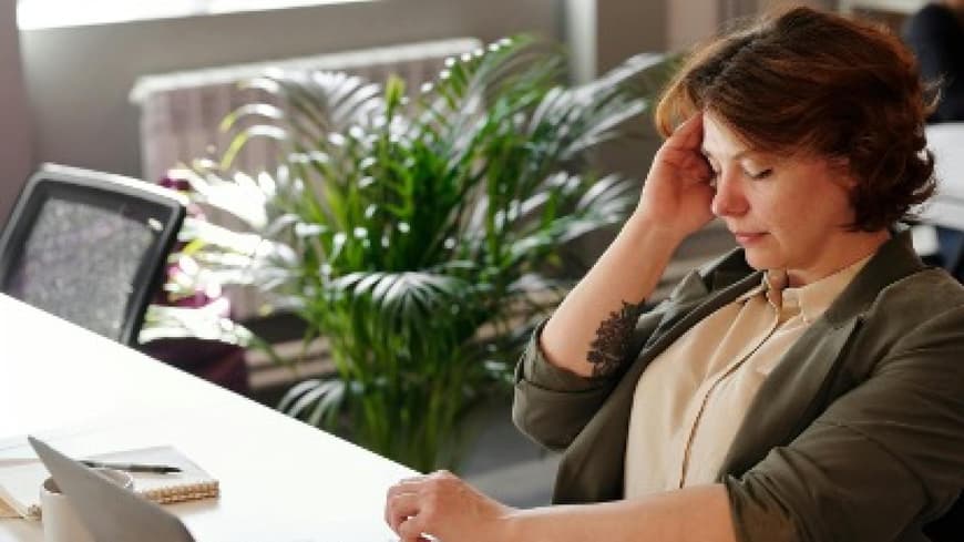 Eine Frau sitzt mit Kopfschmerzen am Schreibtisch