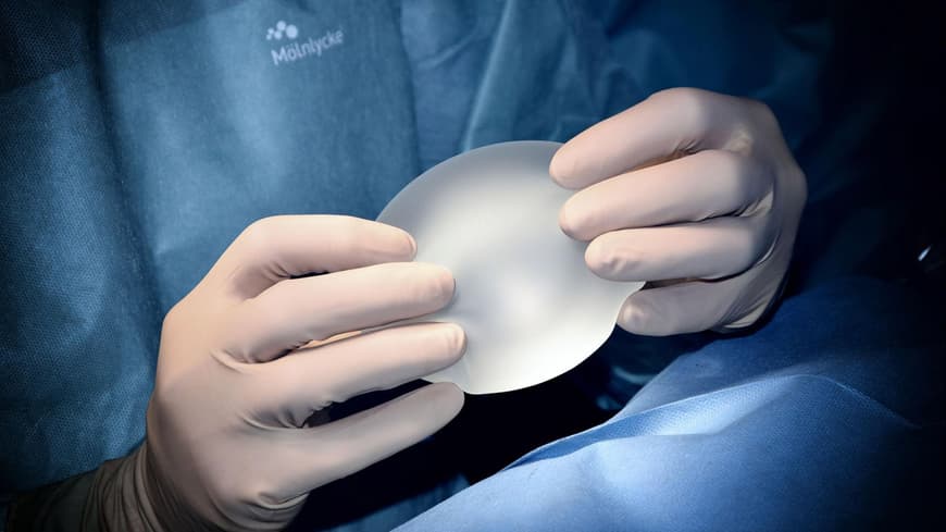 Ein Chirurg hält ein Brustimplantat in den Händen