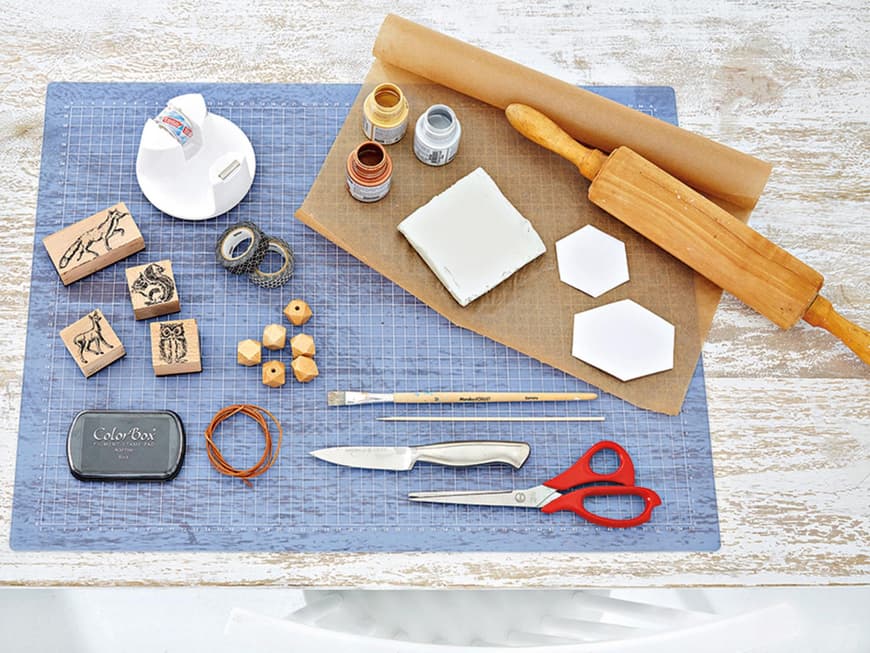 Zum Basteln benötigen Sie: Modelliermasse, Teigrolle, Backpapier, Metallicfarben, Tierstempel, Schere, Messer, Pinsel, Holzperlen, Feines Lederband, Deko-Tape (z.B. von Tesa)