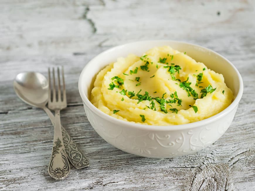In einer Porzellanschüssel angerichtetes Kartoffelpüree auf einem rustikalen Holztisch