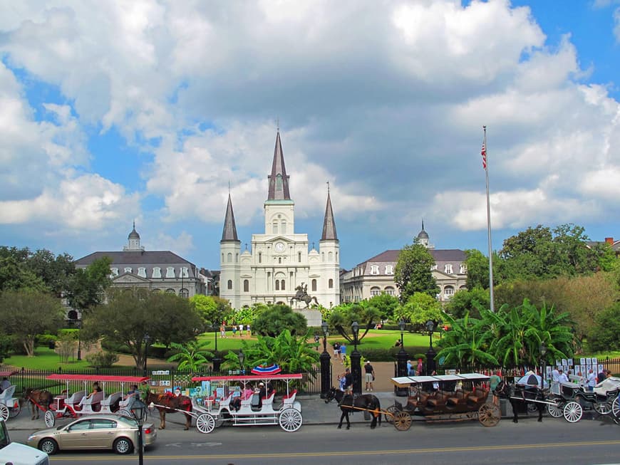 Begrünter Platz namens "Jackson Square" mit rot-weißen Pferdekutschen davor und der weißen St.-Louis-Kathedrale mit drei spitzen Türmen