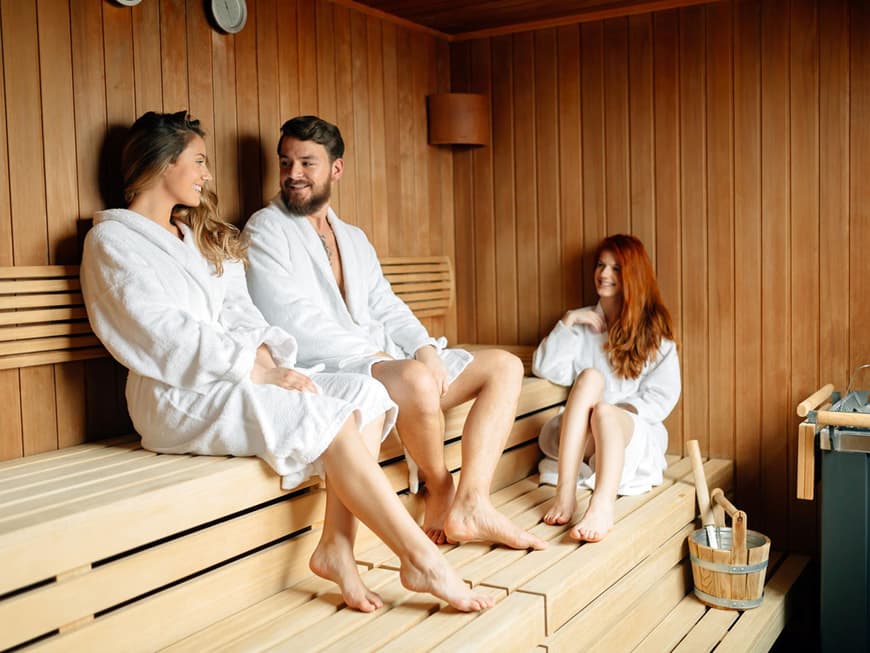 Zwei Frauen und ein Mann in Bademänteln in der Sauna