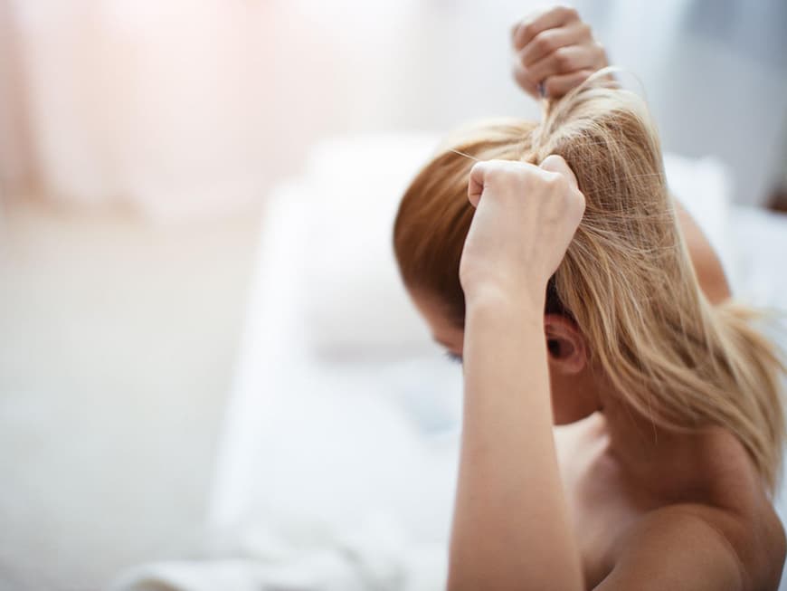 Frau mit langen Haaren macht sich einen Zopf 