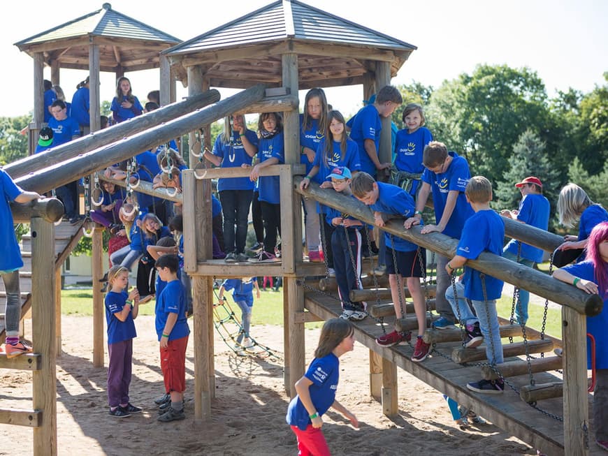 Zahlreiche Kinder in blauen T-Shirts der deutschen Fernsehlotterie auf einem Klettergerüst