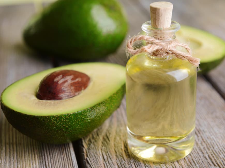 Ein Glas mit Avocado-Öl vor einer frischen, halbierten Avocado