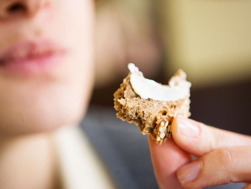 Ein kleines Stück Brot mit Butter bestrichen vor einem Mund