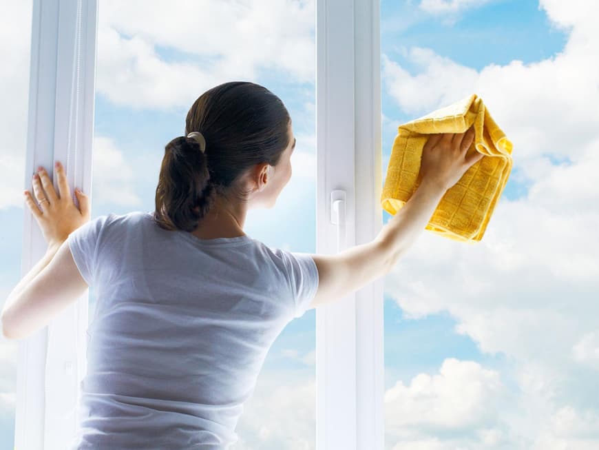 Frau putzt Fenster mit Ausblick auf Wolken am Himmel
