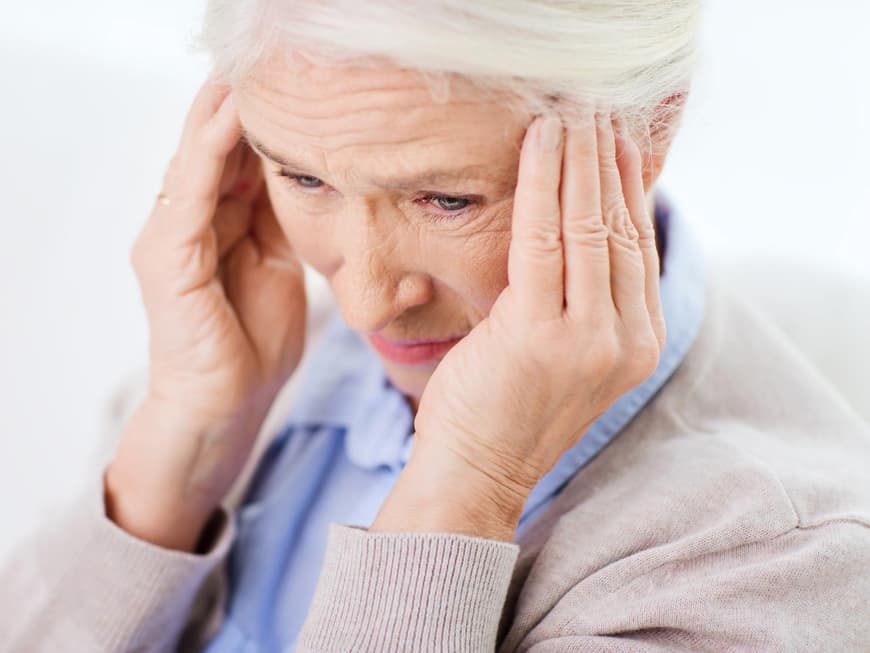 Eine Seniorin hält sich den Kopf vor starken Schmerzen