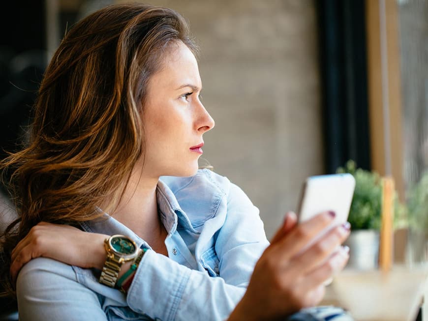 Brünette Frau mit Handy in der Hand blickt ernst in die Ferne