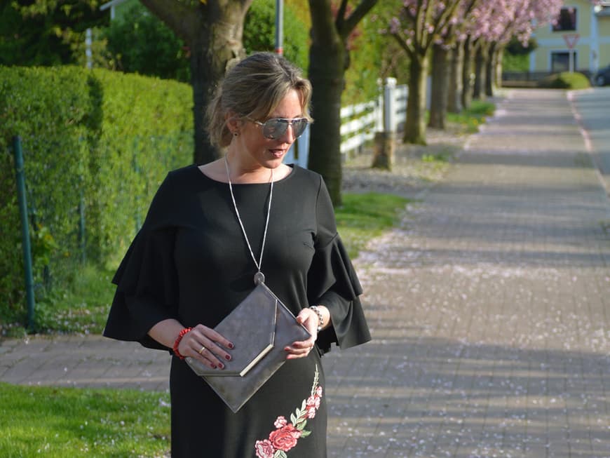 Attraktive Frau mittleren Alters in schwarzem Blumenkleid und Overknee-Stiefeln