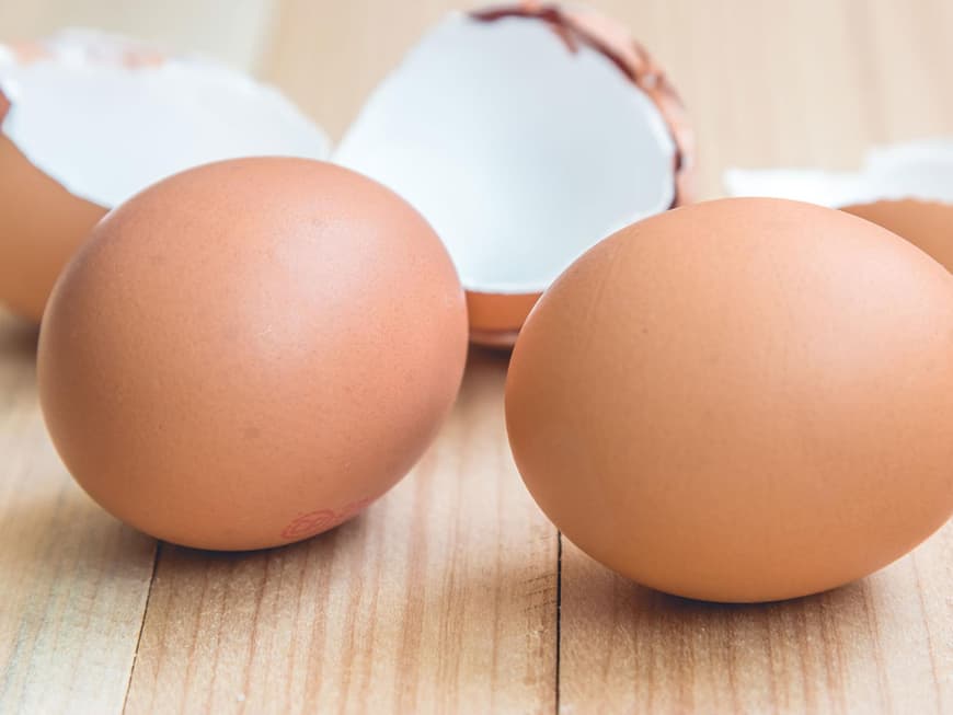 Zwei braune Eier und Eierschale auf einem Holztisch