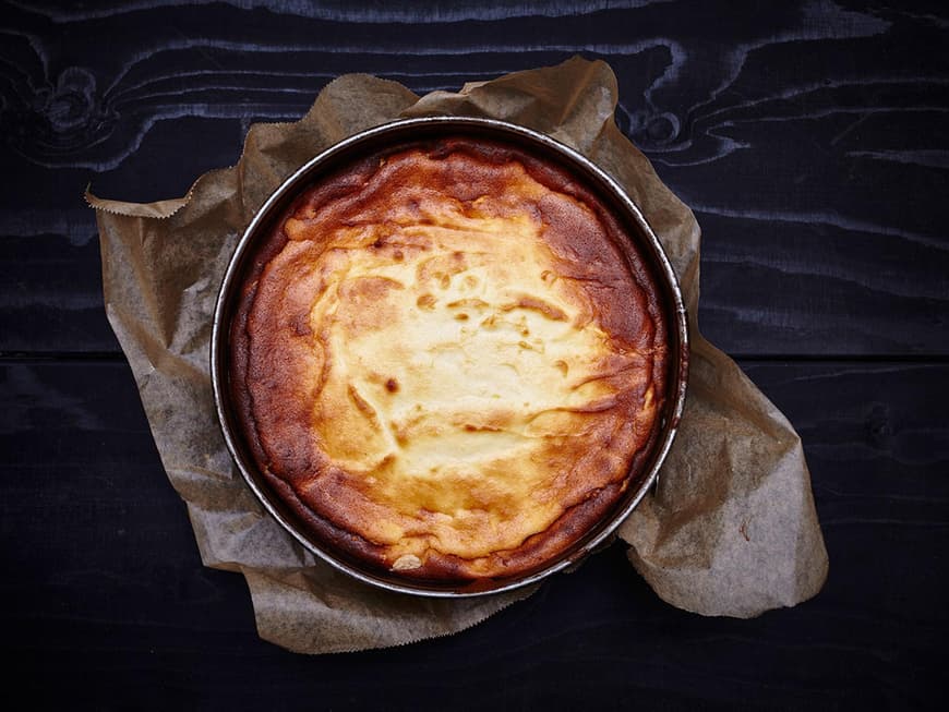Käsekuchen von oben in Springform mit Backpapier auf dunklem Holztisch