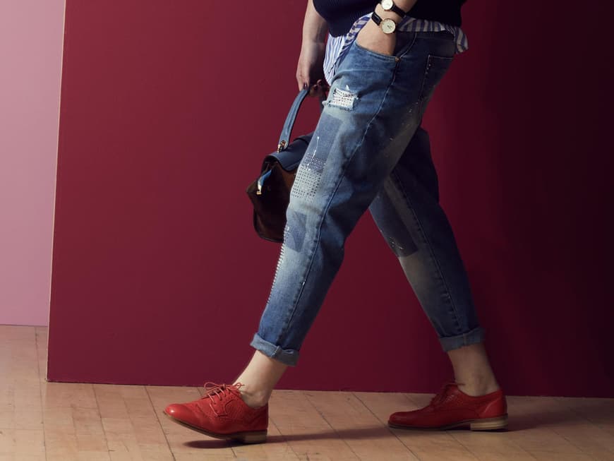 Daniela trägt rote Schnürschuhe zur weiten Jeans und Streifenhemd unterm dunkelblauen Pullunder