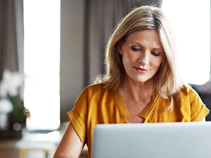 Blonde Frau mittleren Alters sieht versonnen auf den Laptop-Bildschirm