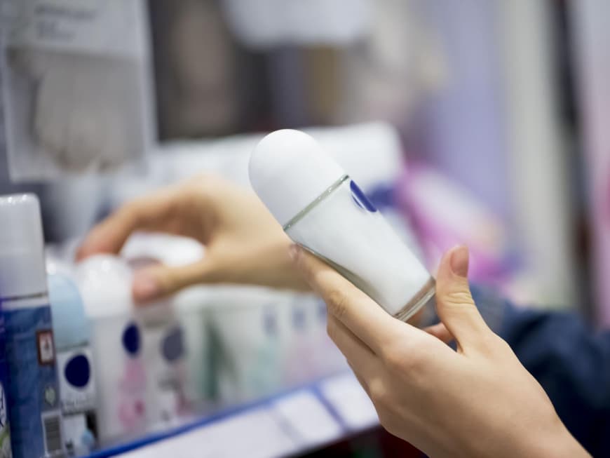 Frau hält ein Deodorant in der Hand vor einem Verkaufsregal