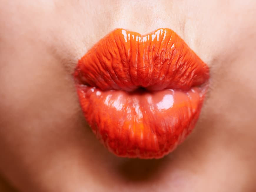 Close-up von gespitzten Lippen mit orangefarbenem Lippenstift