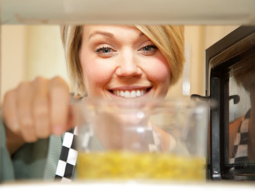 Blonde Frau holt Vorratsdose mit Essen aus der Mikrowelle