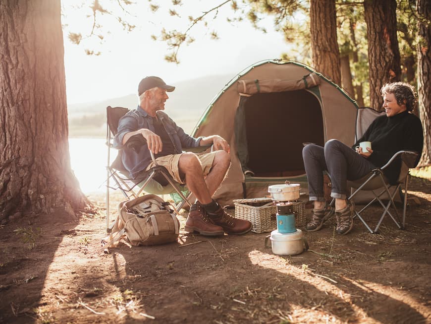 Paar mittleren Alters sitzt auf Campingstühlen vor einem Zelt am See