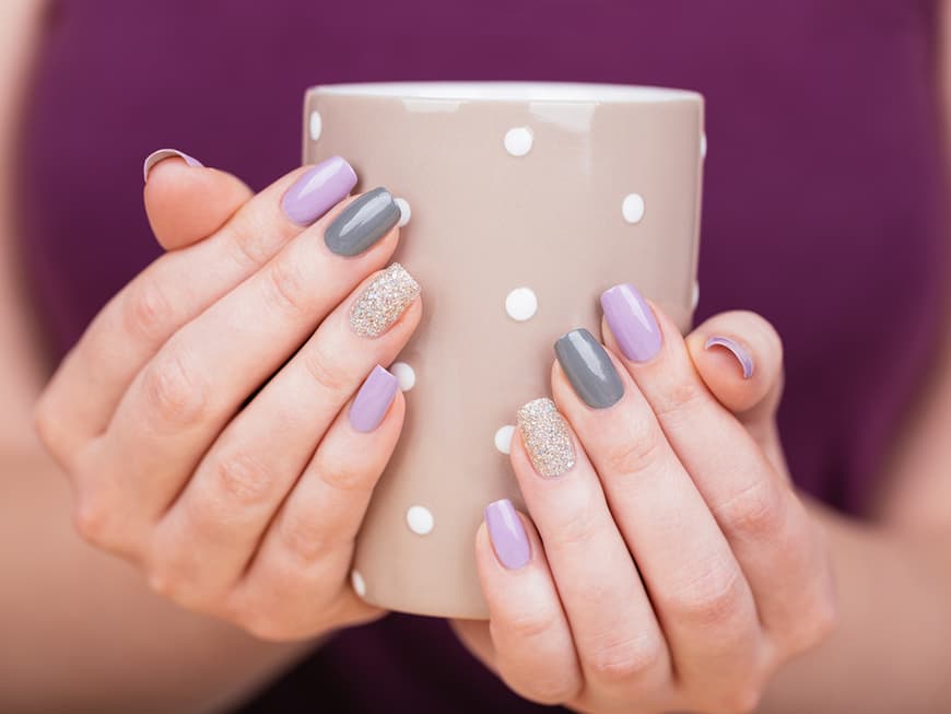 Hände mit verschieden lackerierten Nägeln umfassen eine Tasse