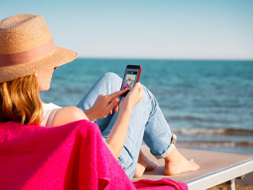 Frau auf einer Liege am Strand mit Handy in der Hand