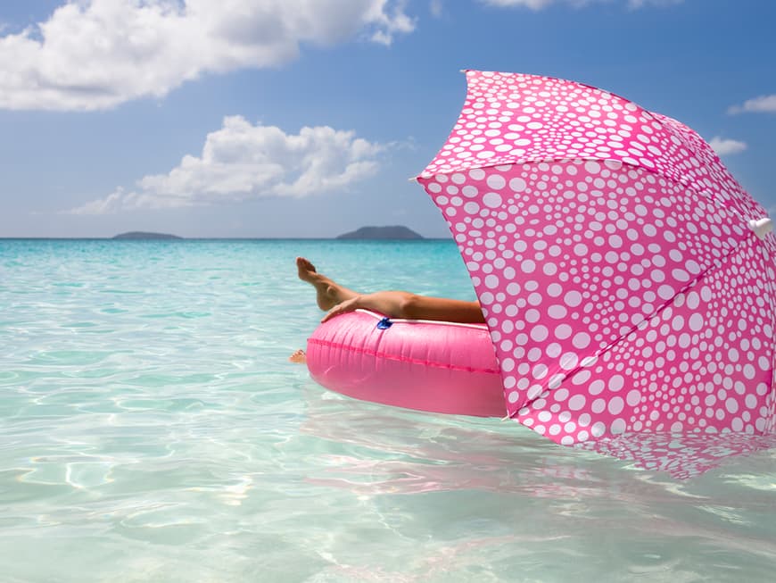 Frau auf pinkfarbenem Schwimmring mit gepunktetem Sonnenschirm in türkisblauem Meer