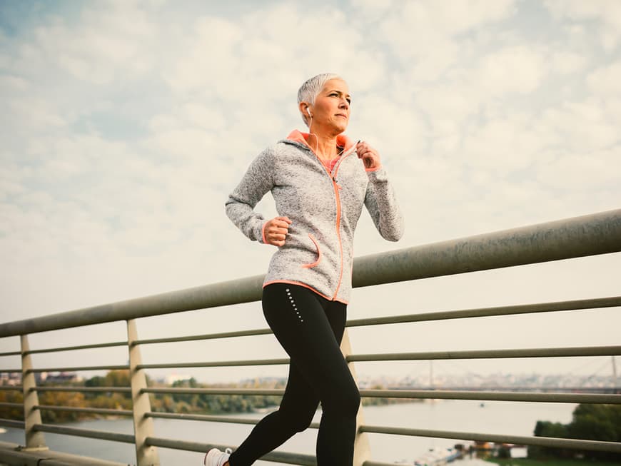 Frau mittleren Alters joggt über eine Brücke