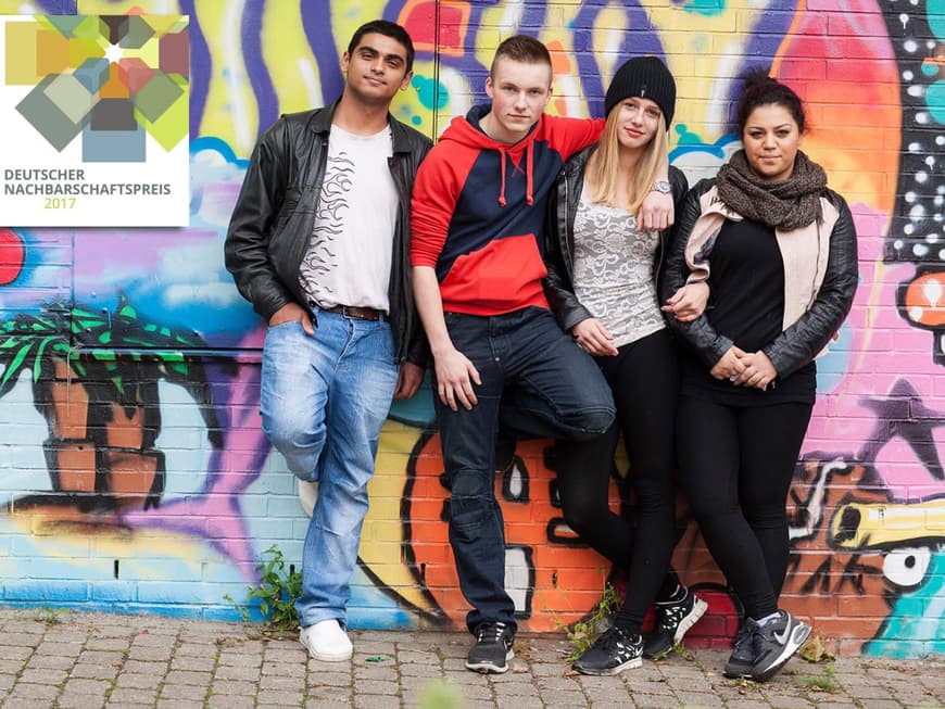 Vier Jugendliche stehen Arm in Arm vor einer besprühten Wand