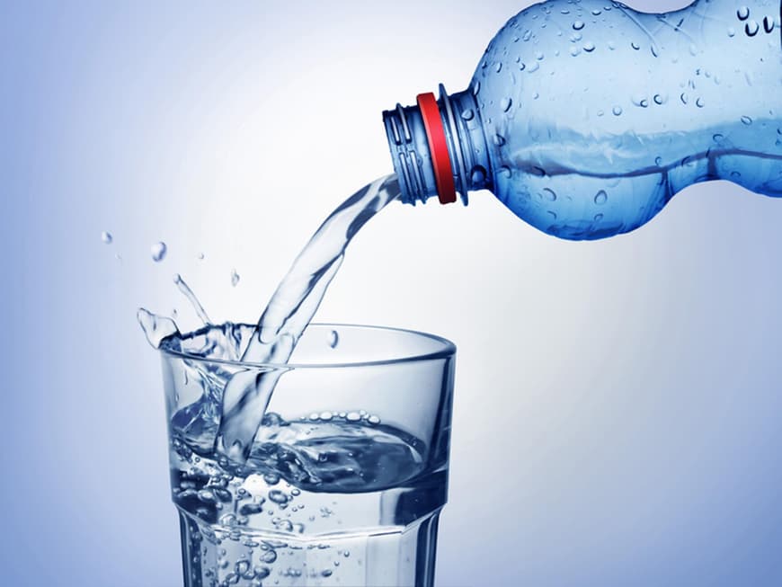Wasser wird von einer Flasche in ein Glas gekippt