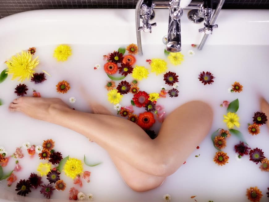 Frauenbeine in einer Badewanne voller Milch mit Blüten