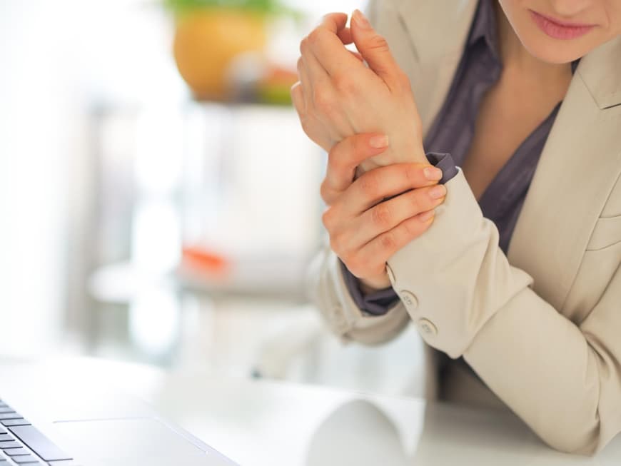 Frau im Businessoutfit hält sich die schmerzende Hand