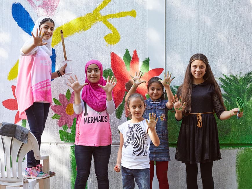 Kinder verschiedener Herkunft mit Pinseln und Farbrollen vor einer bemalten Gartenmauer