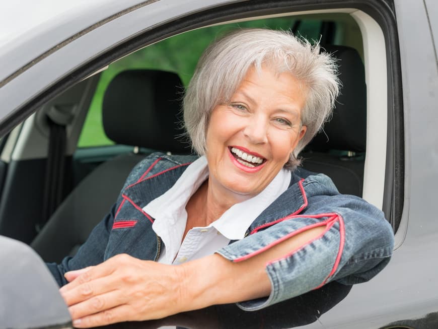 Seniorin lachend am Steuer eines Autos
