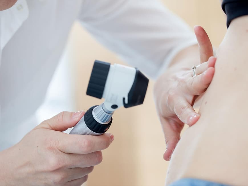 Mit einer Lupe wird die Haut einer Patientin untersucht