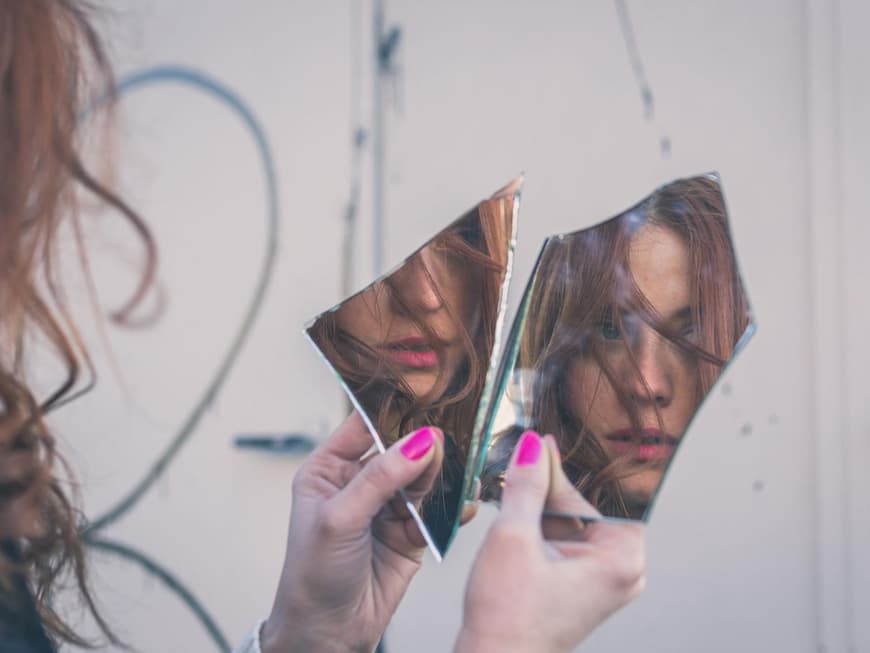 Hübsche junge Frau sieht ihr Spiegelbild in Scherben von Spiegel