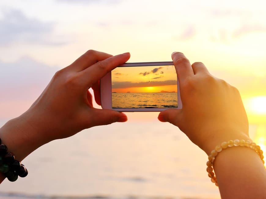 Hände mit Handy beim Fotografieren des Sonnenuntergangs