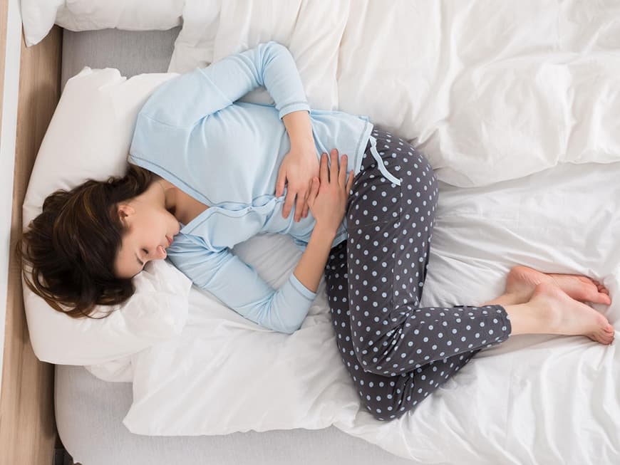 Frau liegt im Bett und hält sich den Bauch
