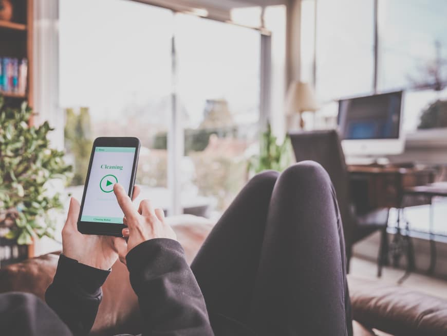Frau bedient vom Sofa aus mit dem Smartphone ihre Technik