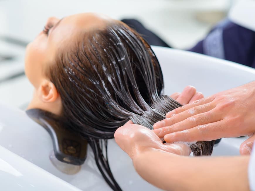 Friseur behandelt Haare einer Frau überm Waschbecken