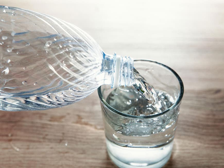 Wasser wird aus einer Plastikflasche in ein Glas gegossen