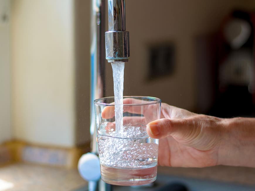 Hand hält Glas unter laufenden Wasserhahn