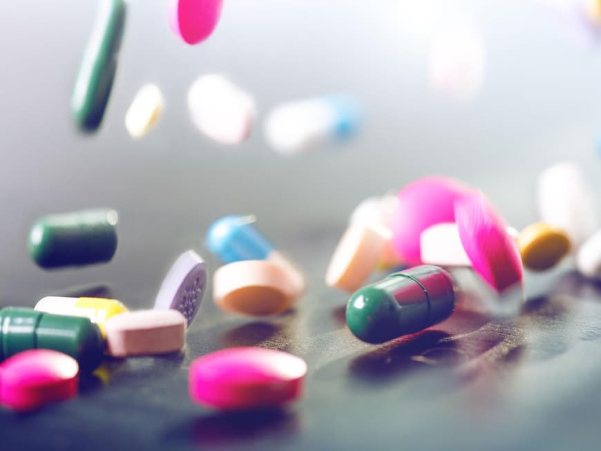 Verschiedene Tabletten und Dragees fallen auf einen Tisch
