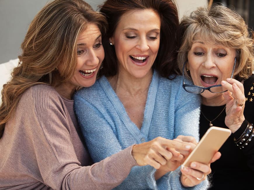 Drei reife Frauen blicken lachend auf ein Smartphone