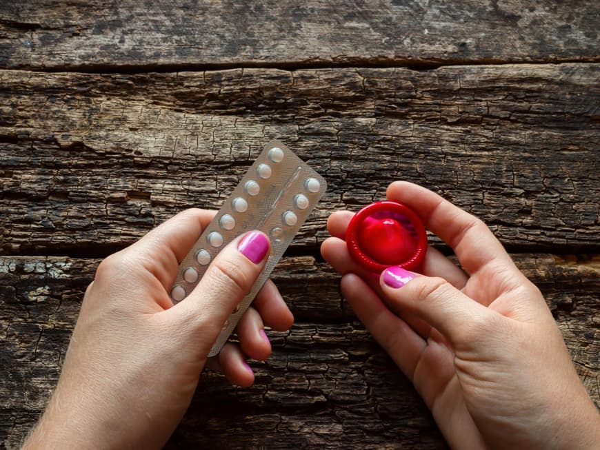 Eine Frau hält ein Kondom sowie einen Blister Pillen in der Hand