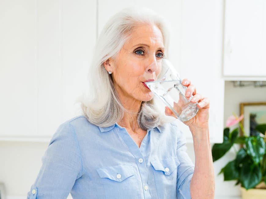 Reife Frau trinkt ein Glas Wasser in der Küche