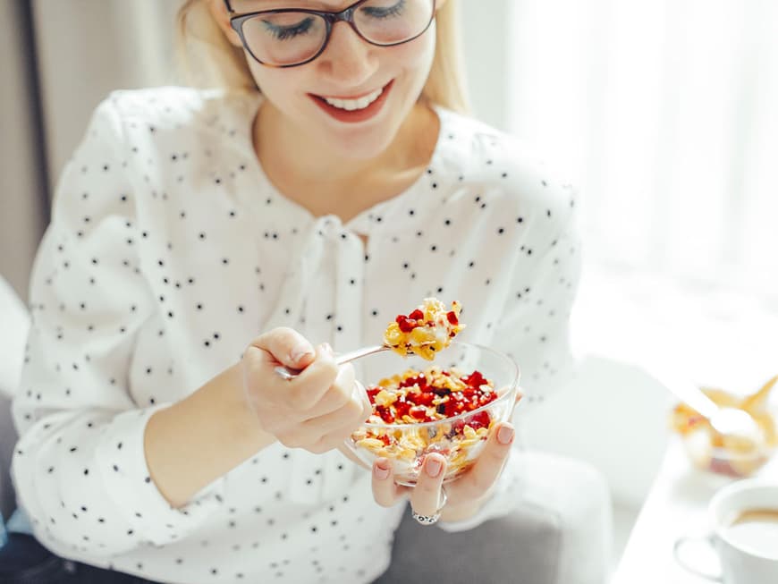 Junge Frau mit Bluse und Brille isst Müsli mit Früchten