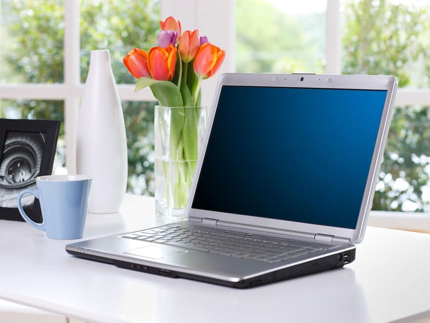 Schreibtisch mit Laptop, Tulpen, Bilderrahmen und Kaffeebecher