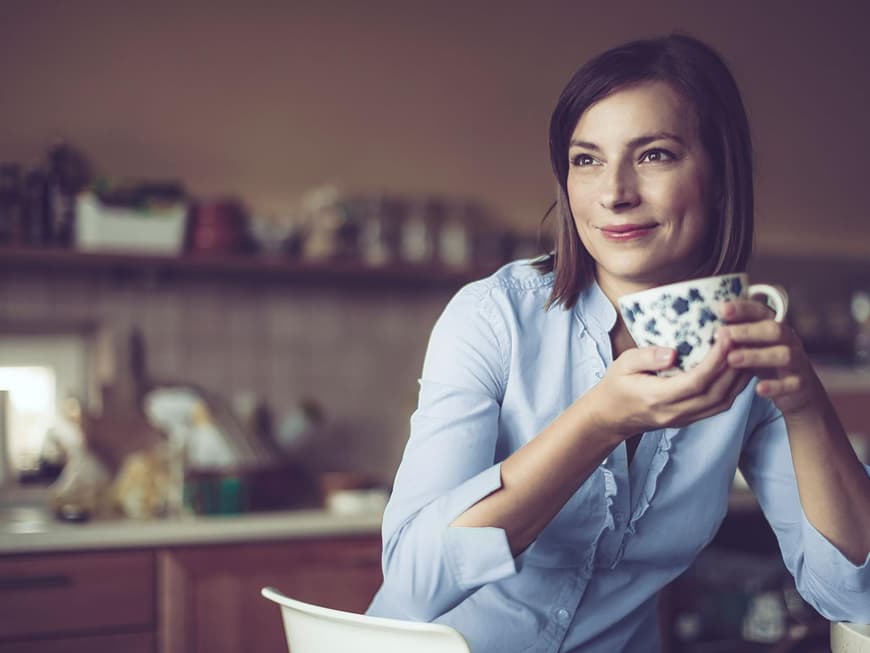 Frau mittleren Alters mit einer Tasse blickt zufrieden in die Ferne