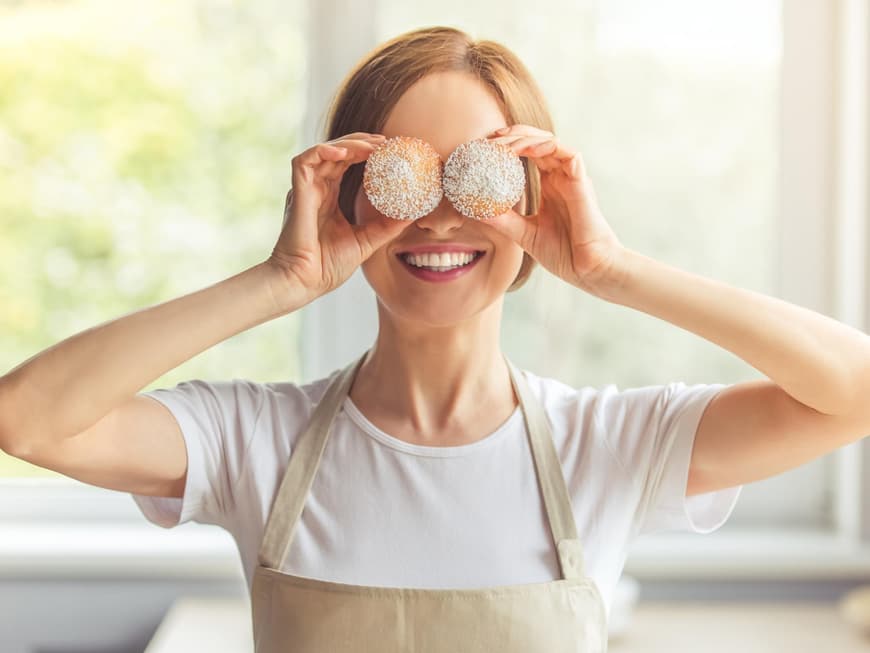 Frau mit Kochschürze hält sich zwei Muffins vor die Augen