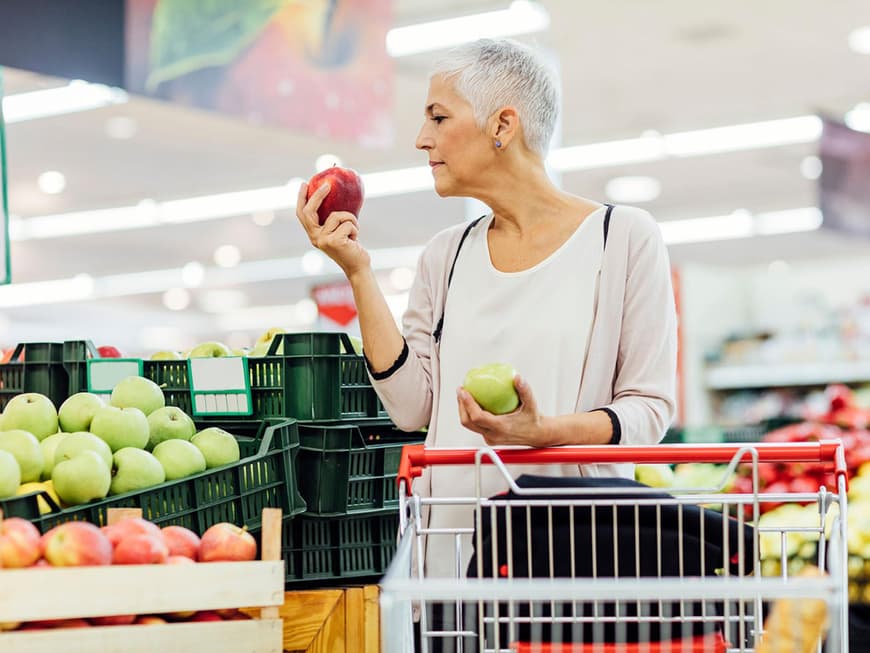Reife Frau hält zwei Äpfel im Supermarkt in den Händen