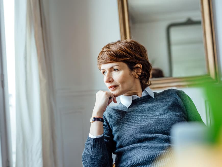 Frau mittleren Alters sitzt nachdenklich auf einem Stuhl